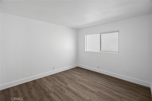 unfurnished room with baseboards and dark wood-type flooring