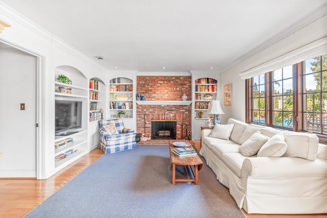 living room with crown molding, built in features, a fireplace, and light wood finished floors