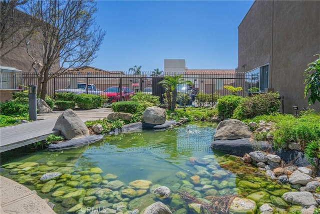 view of community featuring a small pond and fence