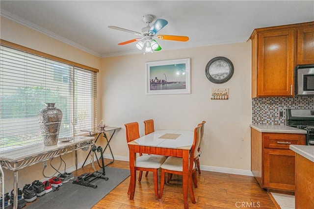 dining area featuring light wood-style floors, baseboards, ornamental molding, and a ceiling fan