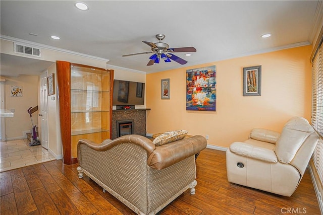 living room with crown molding, ceiling fan, wood-type flooring, baseboards, and visible vents