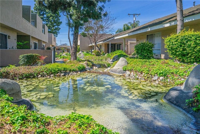 view of community featuring fence and a garden pond