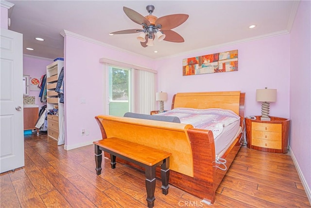 bedroom with a walk in closet, crown molding, baseboards, wood-type flooring, and recessed lighting