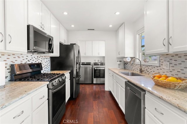 kitchen featuring white cabinetry, washing machine and clothes dryer, light stone counters, a sink, and appliances with stainless steel finishes