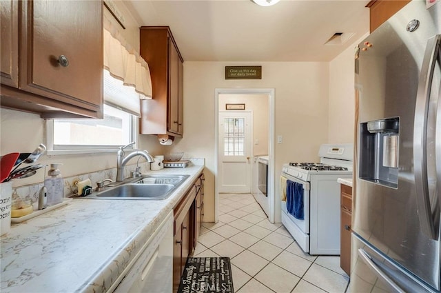 kitchen with a sink, stainless steel fridge, light countertops, white gas range oven, and light tile patterned floors