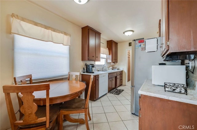 kitchen featuring dishwasher, light countertops, brown cabinets, a sink, and light tile patterned floors