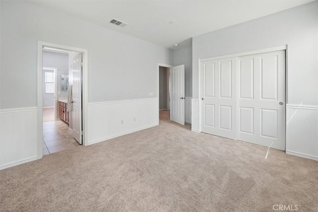 unfurnished bedroom featuring a closet, visible vents, light carpet, and a wainscoted wall