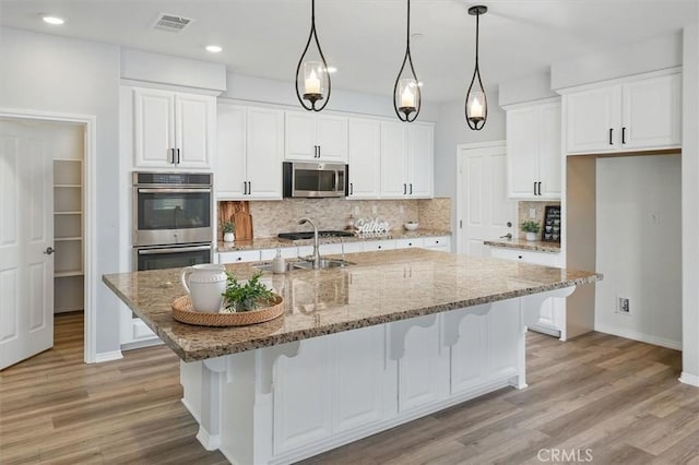 kitchen with white cabinets, backsplash, stainless steel appliances, and light wood-type flooring