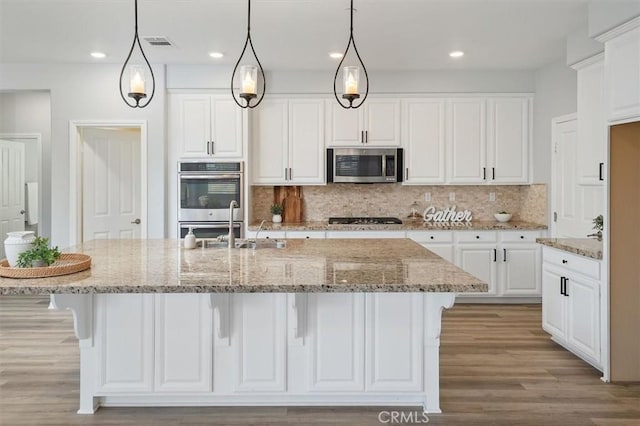 kitchen featuring visible vents, an island with sink, white cabinets, backsplash, and stainless steel appliances