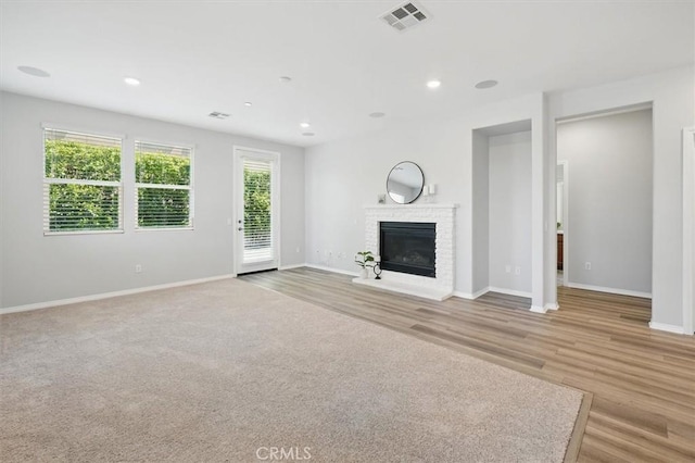 unfurnished living room with a brick fireplace, baseboards, visible vents, and light wood-style floors