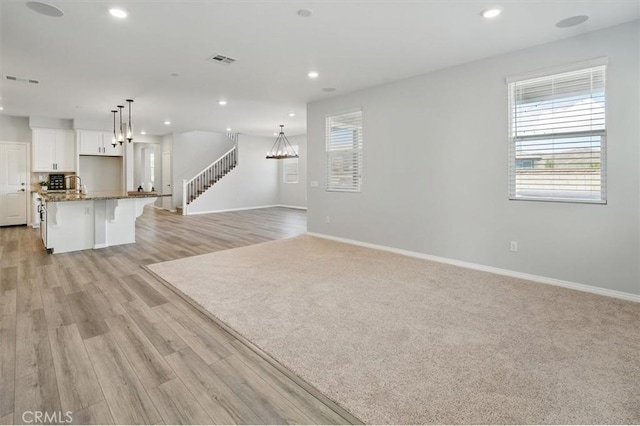 unfurnished living room with baseboards, a notable chandelier, light wood-style flooring, and visible vents