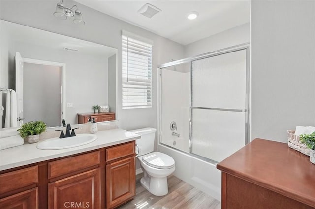 bathroom featuring vanity, shower / bath combination with glass door, wood finished floors, and toilet
