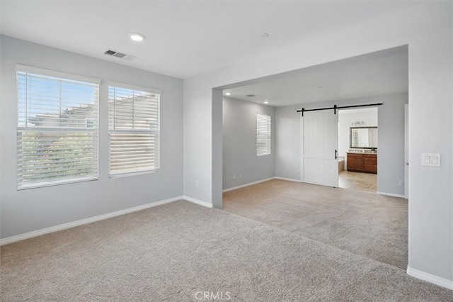 unfurnished room with visible vents, a barn door, baseboards, light carpet, and recessed lighting