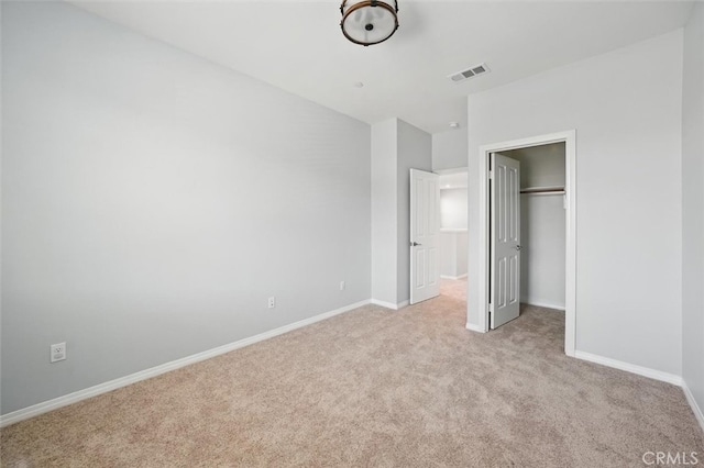 unfurnished bedroom featuring a walk in closet, light colored carpet, visible vents, baseboards, and a closet