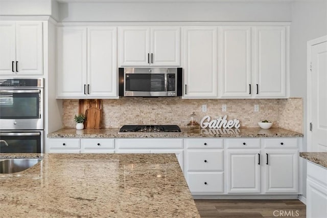 kitchen with decorative backsplash, white cabinetry, light stone counters, a sink, and appliances with stainless steel finishes