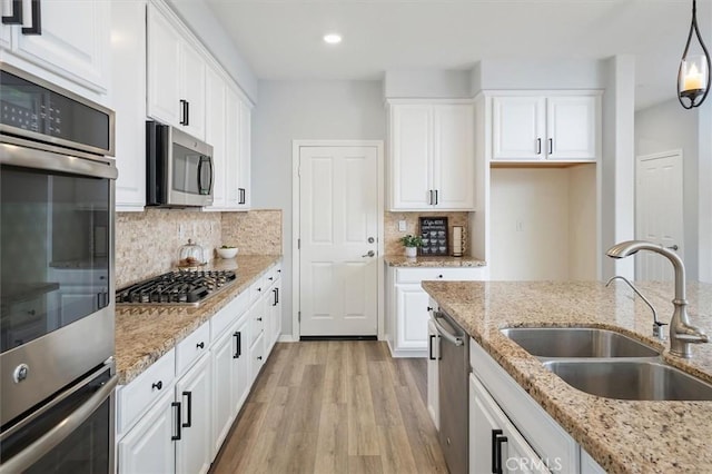 kitchen with white cabinets, appliances with stainless steel finishes, a sink, light wood finished floors, and decorative backsplash