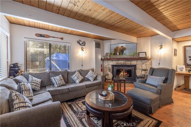 living area with beam ceiling, a stone fireplace, a healthy amount of sunlight, wood finished floors, and wood ceiling