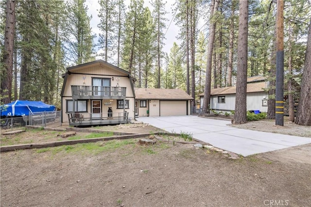 view of front of house featuring an attached garage, a balcony, fence, and driveway