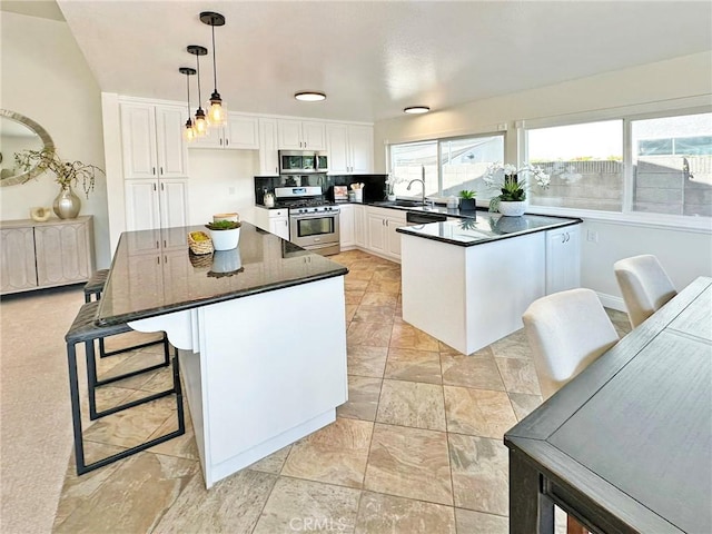 kitchen featuring pendant lighting, dark countertops, white cabinets, a sink, and appliances with stainless steel finishes