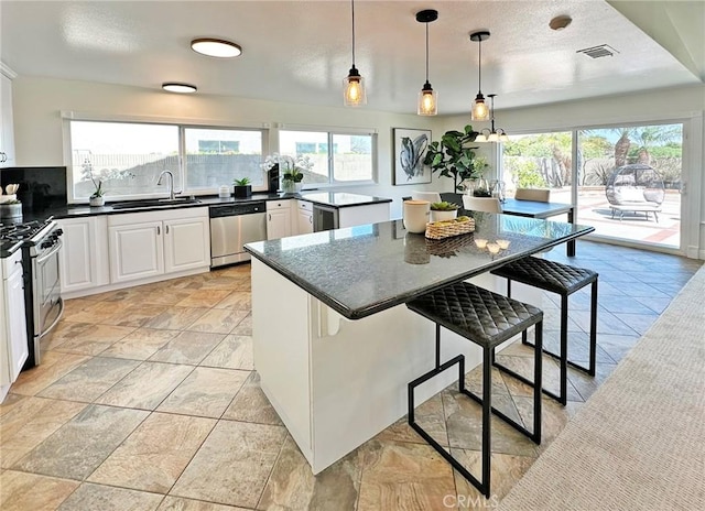 kitchen featuring a breakfast bar area, visible vents, appliances with stainless steel finishes, dark countertops, and a sink