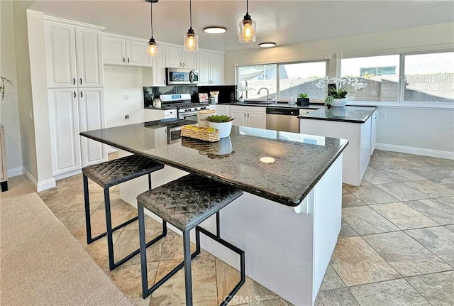 kitchen featuring dark countertops, a sink, stainless steel appliances, white cabinetry, and baseboards