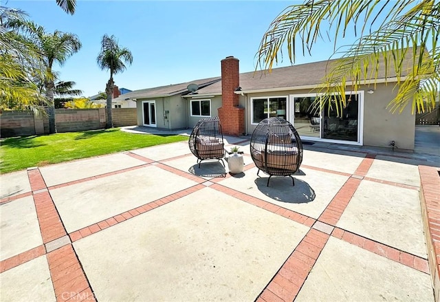 rear view of property featuring fence, stucco siding, a chimney, a patio area, and a yard
