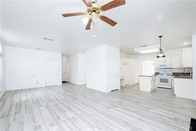 unfurnished living room featuring a sink, light wood-style floors, a ceiling fan, baseboards, and visible vents