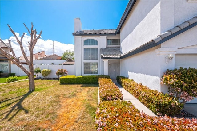exterior space featuring a tiled roof, a chimney, fence, a front lawn, and stucco siding