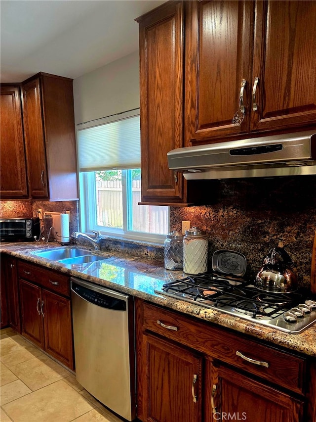 kitchen featuring backsplash, appliances with stainless steel finishes, a sink, stone counters, and under cabinet range hood