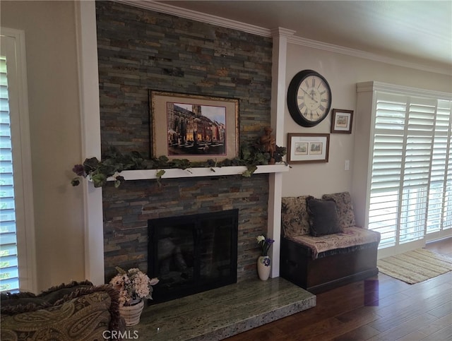 living area with ornamental molding, a stone fireplace, and wood finished floors