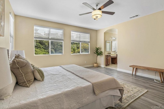 bedroom with visible vents, wood finished floors, baseboards, arched walkways, and ensuite bath