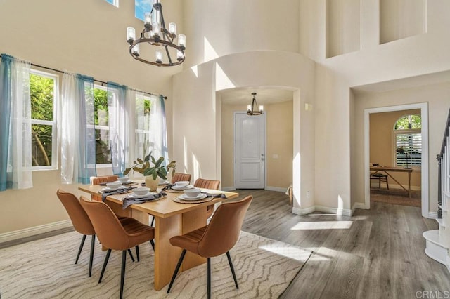 dining room featuring baseboards, a towering ceiling, wood finished floors, and a chandelier