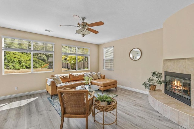 living room featuring light wood-style floors, baseboards, a tiled fireplace, and a ceiling fan
