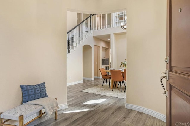 foyer entrance featuring arched walkways, baseboards, wood finished floors, and a towering ceiling