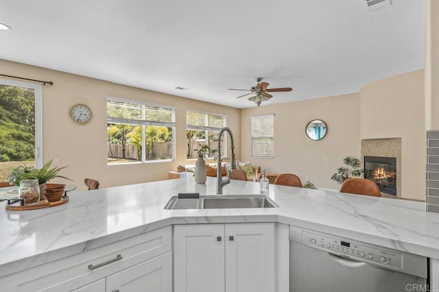 kitchen with a fireplace, light stone countertops, ceiling fan, a sink, and dishwasher