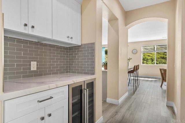 kitchen with beverage cooler, white cabinets, arched walkways, light wood finished floors, and backsplash