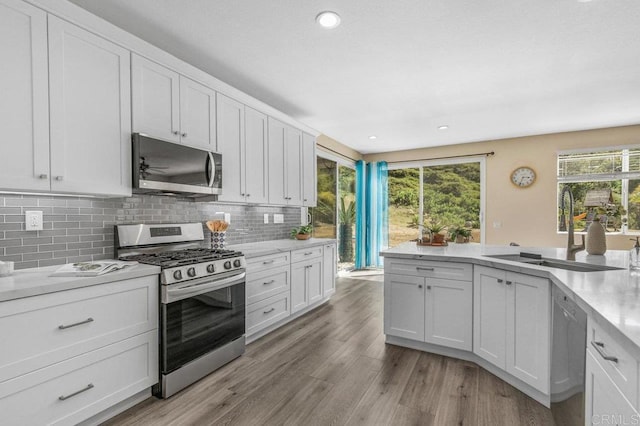 kitchen with decorative backsplash, white cabinets, a sink, light wood-style flooring, and appliances with stainless steel finishes
