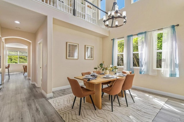 dining area featuring an inviting chandelier, arched walkways, baseboards, wood finished floors, and a towering ceiling