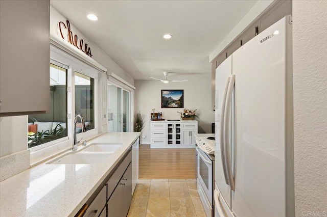 kitchen featuring light stone countertops, ceiling fan, a sink, white appliances, and recessed lighting
