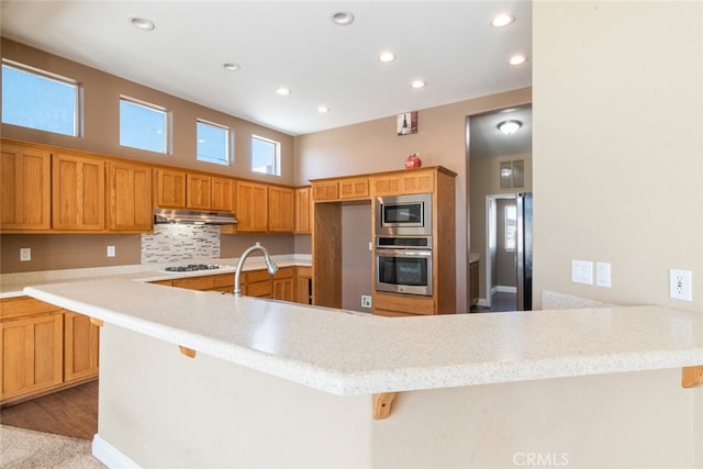 kitchen featuring a peninsula, recessed lighting, light countertops, under cabinet range hood, and appliances with stainless steel finishes