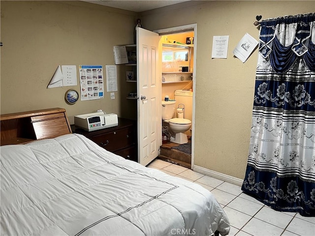 bedroom featuring baseboards, light tile patterned floors, and ensuite bath