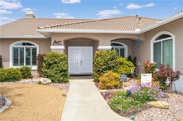 view of exterior entry with a tiled roof, a chimney, and stucco siding