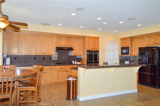 kitchen featuring ceiling fan, a kitchen breakfast bar, black appliances, under cabinet range hood, and light wood-style flooring