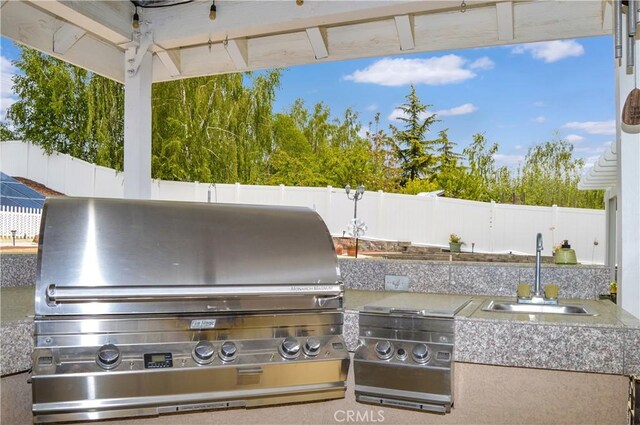 view of patio featuring a fenced backyard, an outdoor kitchen, a sink, and area for grilling