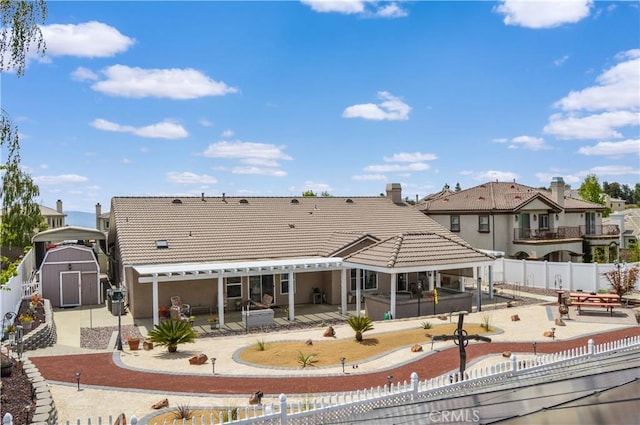 back of property featuring a tile roof, a storage shed, an outbuilding, a patio area, and a fenced backyard