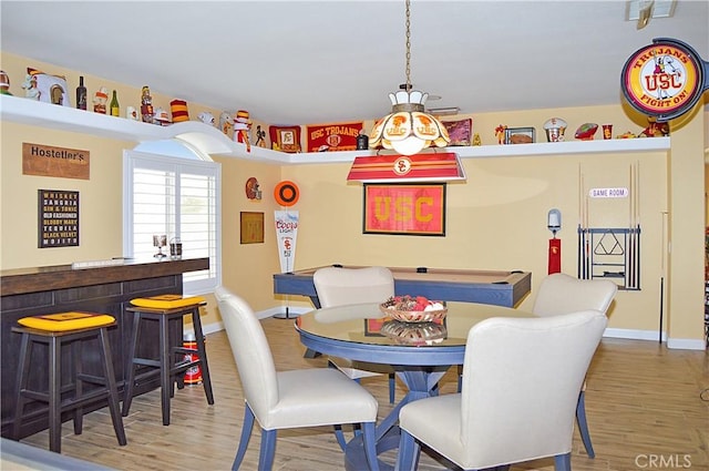 dining space with baseboards, bar area, and wood finished floors