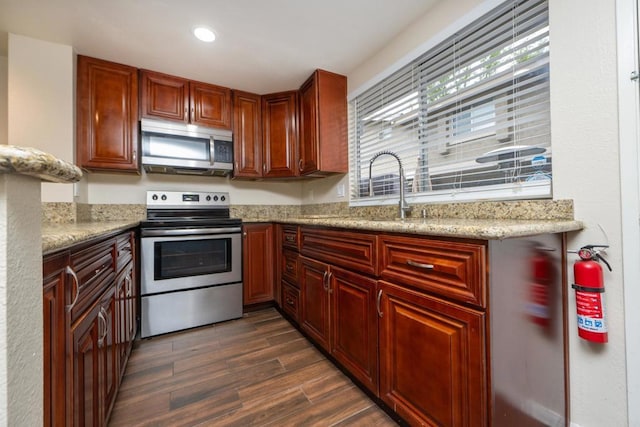 kitchen with light stone counters, a sink, dark wood finished floors, stainless steel appliances, and recessed lighting