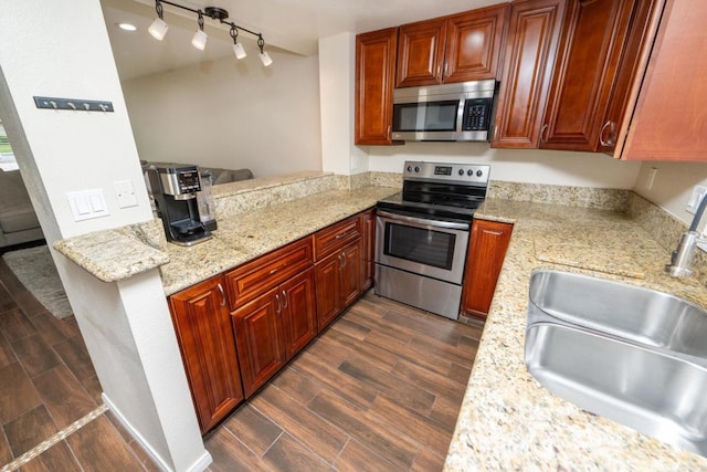 kitchen with track lighting, dark wood-style flooring, light stone counters, a sink, and appliances with stainless steel finishes