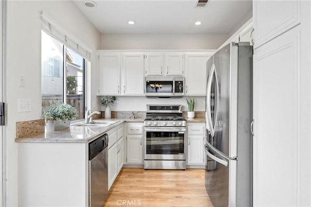 kitchen with light stone countertops, light wood-type flooring, white cabinetry, a sink, and stainless steel appliances