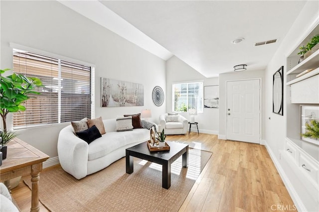 living area featuring baseboards, visible vents, vaulted ceiling, and light wood-style floors